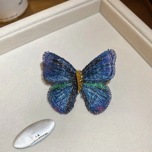 Detailed view of an embroidered butterfly brooch with blue and green gradient silk wings