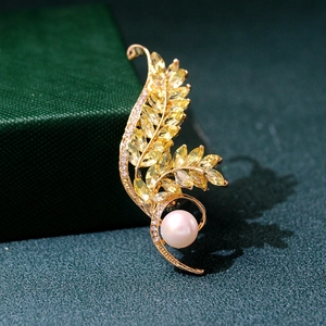 Detailed macro view of golden leaf brooch with yellow zircons and white pearl on green box