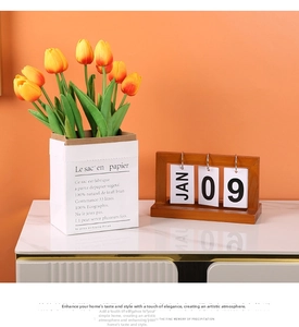 Detail of wooden flip calendar with orange tulips in a white paper bag vase on marble