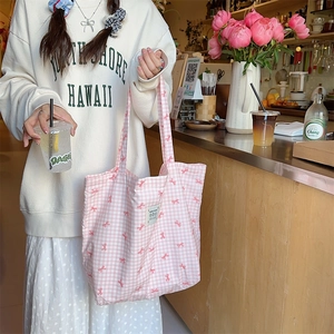 Pink checkered canvas tote bag with red ribbon prints held in a cozy cafe setting