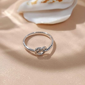 Elegant silver love knot ring in stainless steel shown on beige silk background