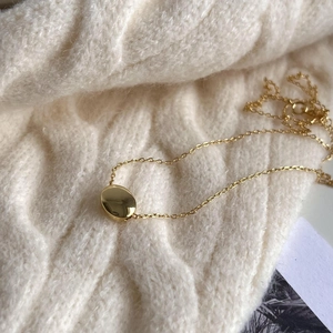 Detail view of a minimal gold 925 sterling silver bean necklace on a knit sweater