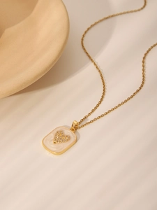 Close-up of heart-shaped zircon pendant on rectangular white enamel and gold chain