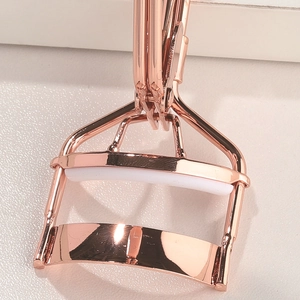 Macro detail of rose gold stainless steel eyelash curler with protective white silicone pad