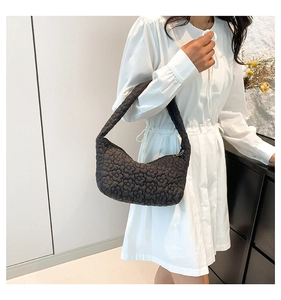 Detail of a black quilted shoulder bag featuring unique 3D floral texture and zipper
