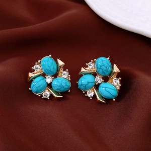 Detailed shot of vintage gold stud earrings with turquoise stones and zircons on silk