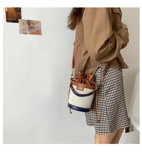 Detail of canvas bucket bag with brown leather trim and adjustable shoulder strap