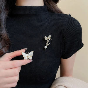 Detail view of 14K gold plated tulip and butterfly brooches with pearls on black knit