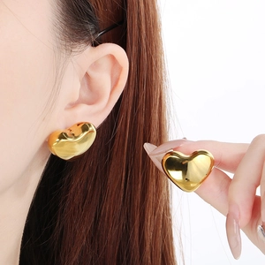 Detail showing polished gold heart stud earrings worn by a model and held for macro view