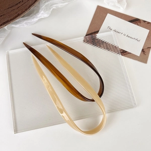 Detail of two U-shaped hair pins in amber and beige finish on minimalist background