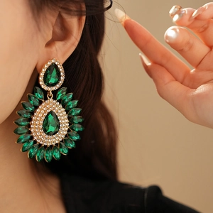 Close-up of green teardrop earrings with gold setting and sparkling crystals on model