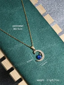 Detail of gold crescent moon pendant with blue glitter sphere and pave zircon on green fabric