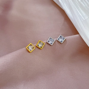 Detailed close-up of square zircon stud earrings in gold and silver on pink silk
