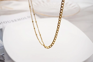 Detail of gold asymmetric chain necklace featuring chunky curb links and round metal disks
