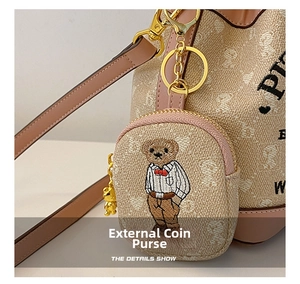 Detail shot of a beige bucket bag featuring a teddy bear embroidered charm and pink leather trim