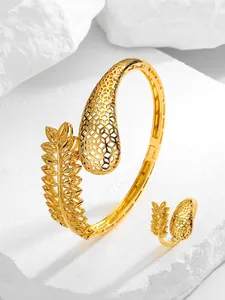 Detail shot of gold-plated leaf and honeycomb open cuff bracelet and ring set on white stone