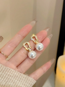 Close-up of a horseshoe-shaped 18K gold-plated earring with zircons and a white pearl