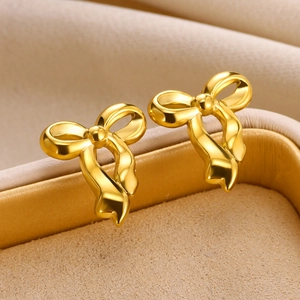 Detailed close-up of shiny gold bow-shaped stud earrings on a beige velvet jewelry box