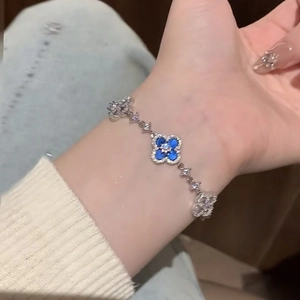 Close-up of a silver-toned clover bracelet featuring a blue gemstone and zircons on a wrist