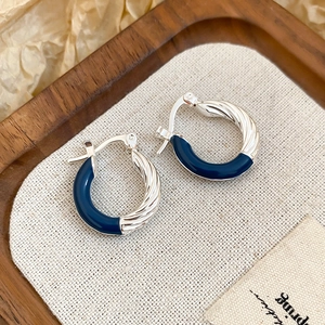 Macro detail of silver hoop earrings with twisted metal texture and deep blue enamel finish