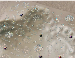Macro view of ocean-themed nail decals with holographic shells and colorful rhinestones