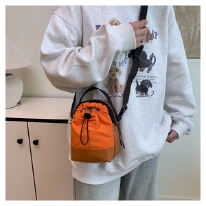 Close-up of orange canvas drawstring crossbody bag with leather trim worn by model