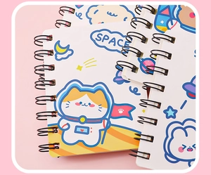 Close-up of stacked A7 spiral notebooks featuring cute cartoon space cat illustrations