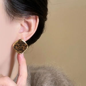 Close-up of square leopard print earrings with gold metal frame worn by a model