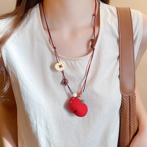 Detail of red apple pendant necklace with woven cord worn on a neutral sweater
