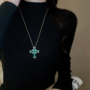 Détail d'un collier pendentif croix dorée avec zircon vert sur col roulé noir