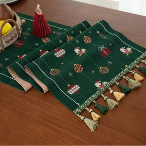 Detail of green Christmas table runner with festive Santa motifs and tassel fringe