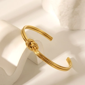 Poliertes Edelstahl-Armreif mit Knotendesign in Gold auf ästhetischem weißem Stein
