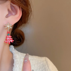 Close-up of sparkling snowflake stud and red Christmas tree pendant earring on a model