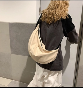 Back view of a beige nylon crossbody bag featuring a soft minimalist crescent design