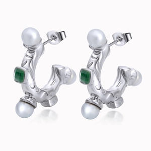 Detail of silver C-shaped earrings with white pearls and green square gemstones