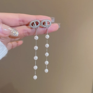 Close-up of dangling zircon earrings featuring a crystal-encrusted CD logo and pearls