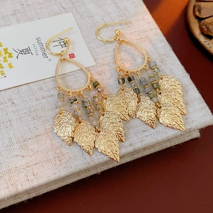 Détail de boucles d'oreilles feuille dorée bohème avec perles colorées sur livre