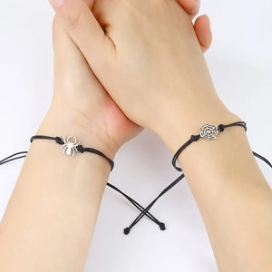 Close-up of couple holding hands wearing black woven spider and web charm bracelets