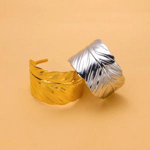 Detail of gold and silver leaf-textured open cuff bracelets on a minimal background