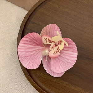 Detailed view of pink Phalaenopsis orchid hair clip on a rustic wooden tray