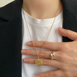 Detailed view of a gold square relief pendant necklace and intertwined mixed metal ring