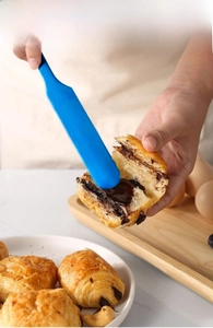 Blue silicone spatula spreading rich chocolate cream on a fresh croissant