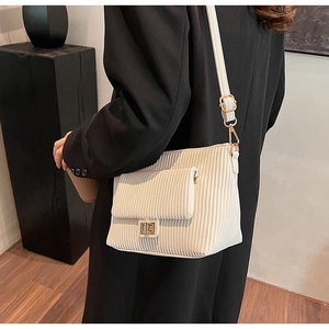 Detail view of cream crossbody bag with corduroy texture and golden turn-lock buckle