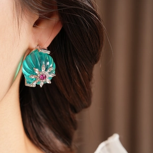 Close-up of vintage flower earrings with green shell and red gemstone on a female model