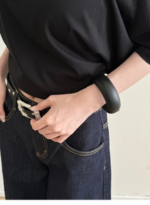 Close-up of a wide matte black bangle styled with a minimalist outfit and vintage belt