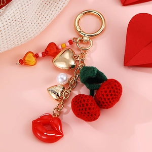 Golden keychain featuring red cherry and lip charms with heart pendants on pink background