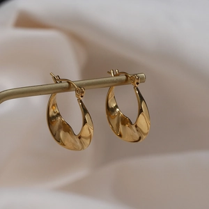 Irregular golden twisted hoop earrings displayed on a minimalist gold stand