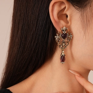 Close-up of vintage heart earrings with purple gems and drop pendants on model