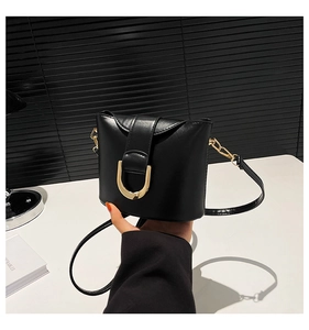 Close-up of golden horseshoe buckle and textured black leather on a designer bucket bag