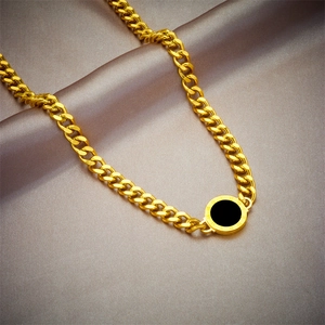 Gold Cuban chain necklace with Roman numeral round pendant on grey fabric background